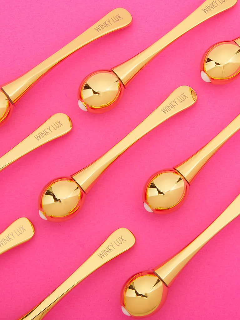 several eye cream applicators lined up lying down on pink background