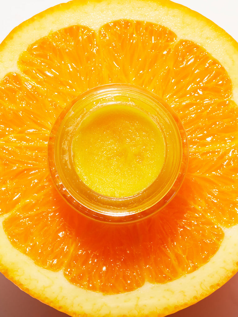 mini orange you bright vitamin c exfoliator sitting on orange slice with lid off