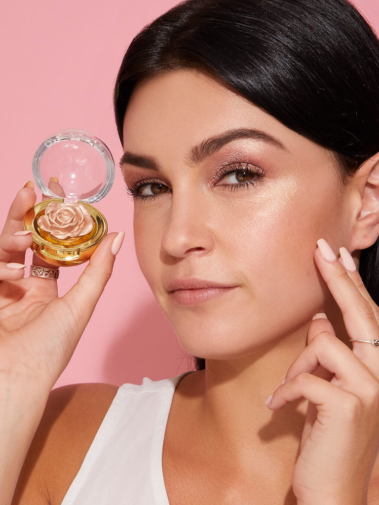 Champagne -- model holding up cheeky rose cream highlighter next to face