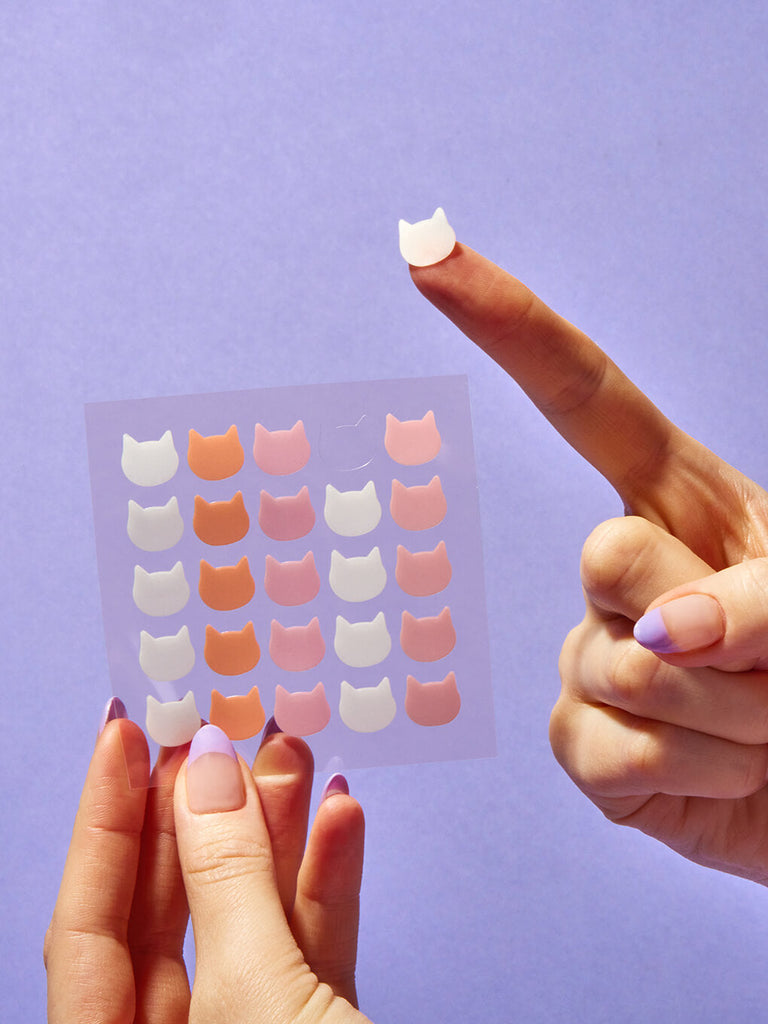 cat shaped pimple patch on model finger on purple background