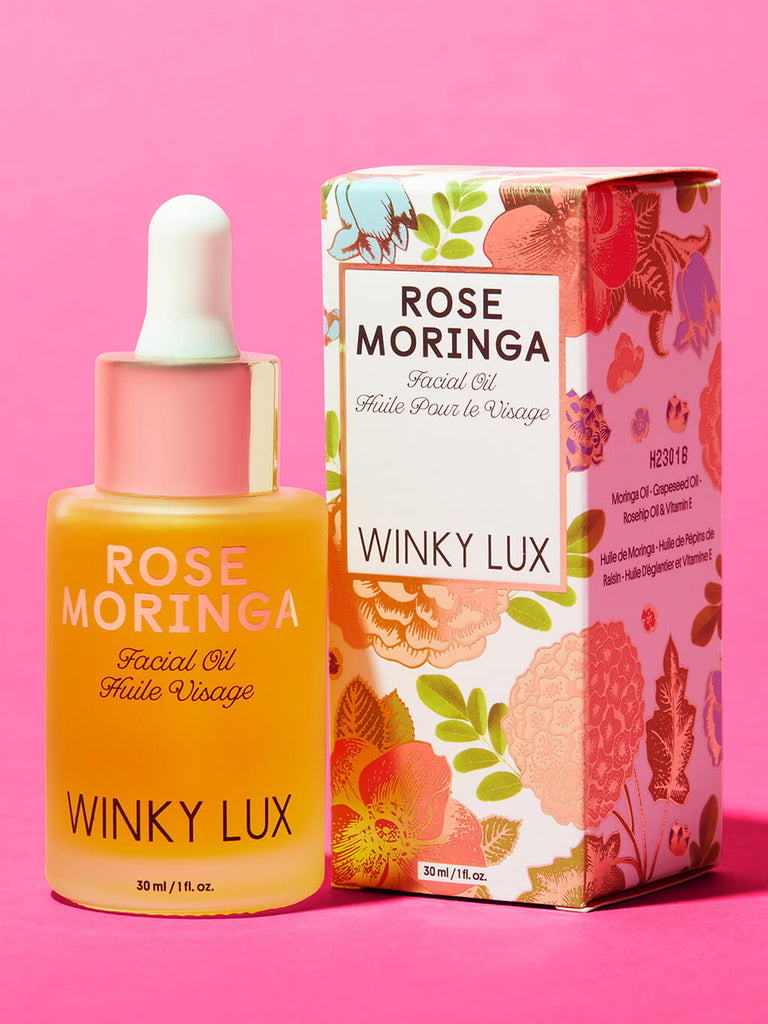 bottle of rose moringa facial oil next to box on pink background