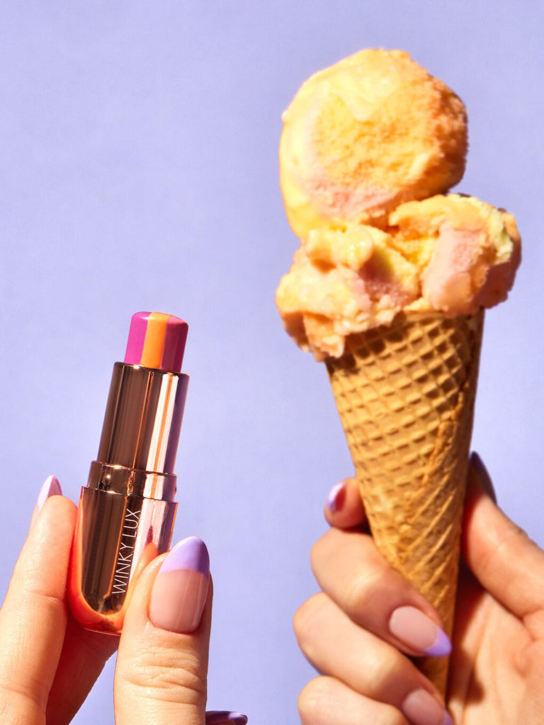 hands holding up sorbet tinted lip balm next to ice cream cone