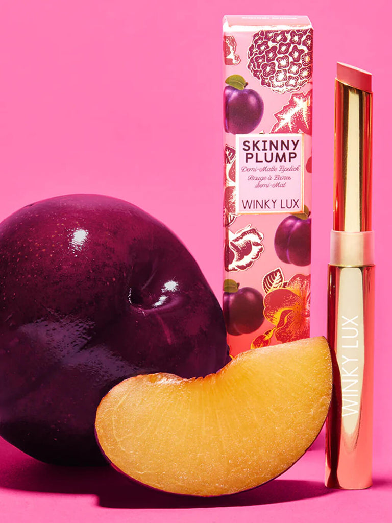 skinny plump demi matte lipstick standing up next to box and plum