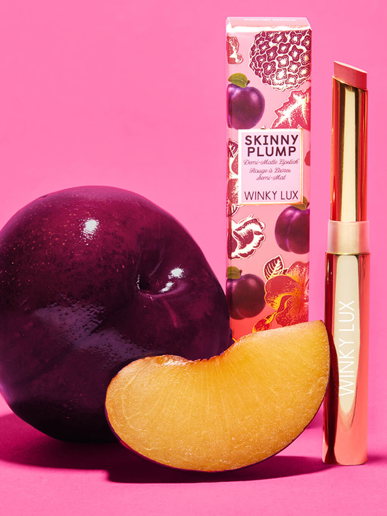 rom com -- skinny plump demi matte plumping lipstick standing next to box and plum