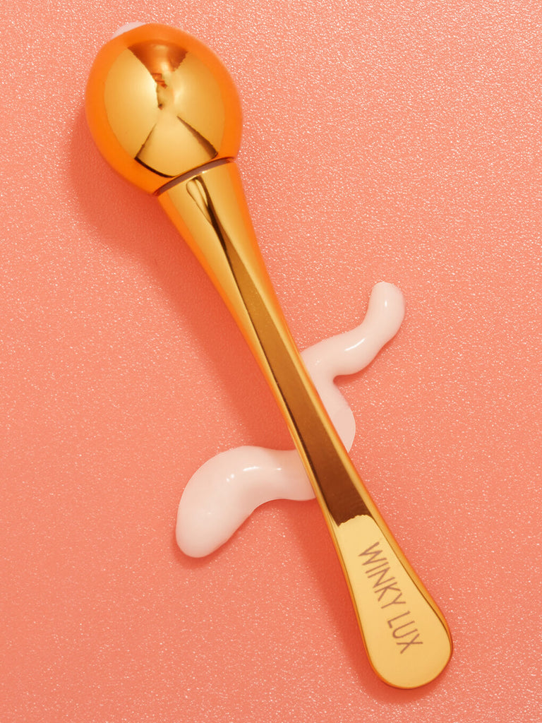 eye cream applicator lying on top of eye cream goop on orange background