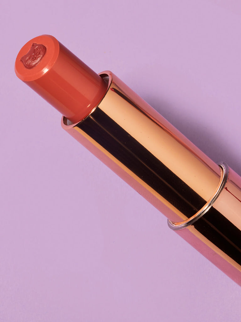 pounce -- close up of purrfect pout sheer lipstick flat lay on purple background