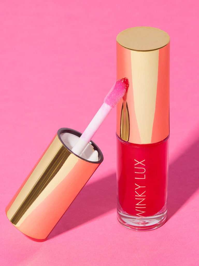 luscious -- barely there tinted lip oil cap leaning against bottle on pink background