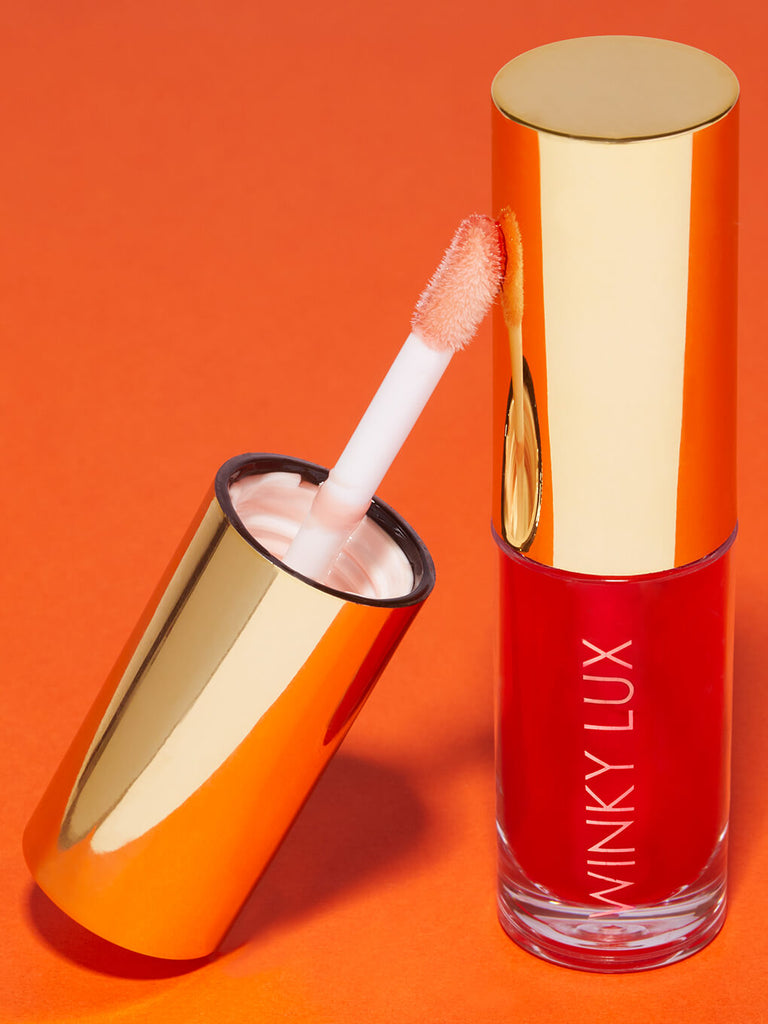 flush -- barely there tinted lip oil cap leaning against bottle on orange background