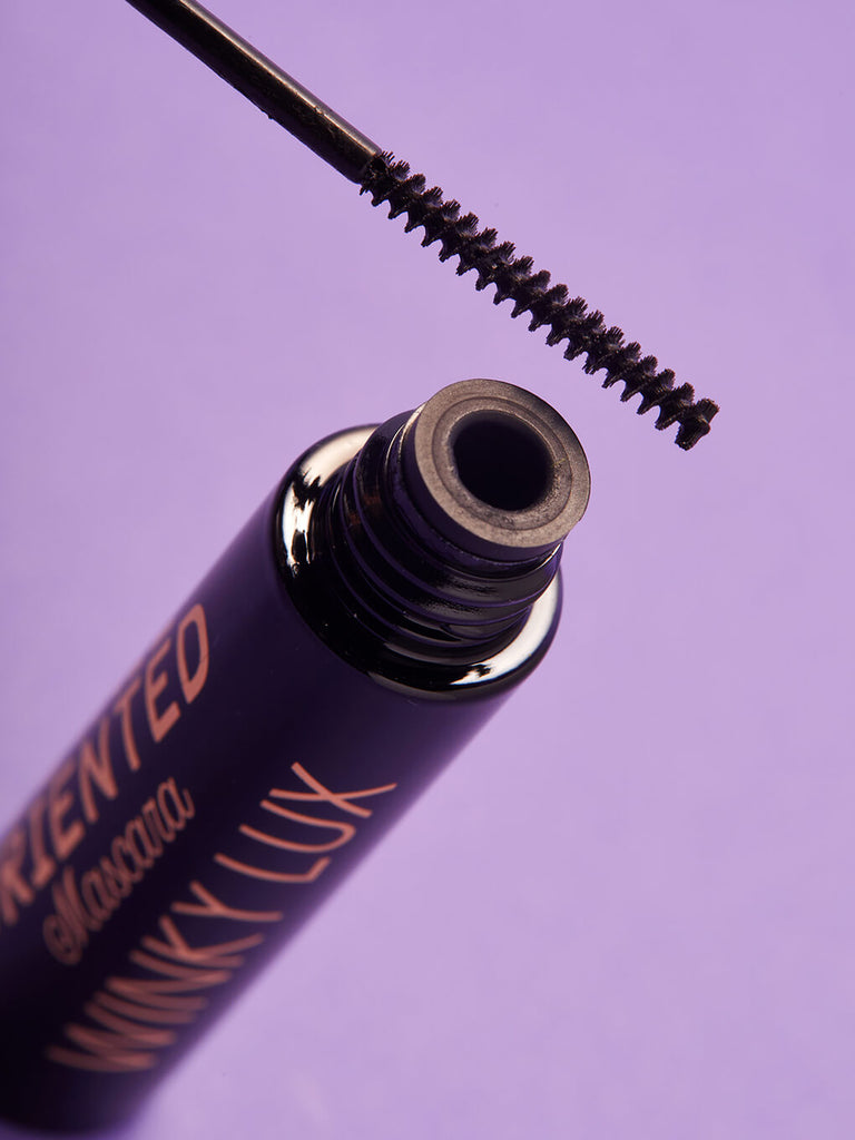close up of detai oriented mascara component and spoolie on purple background