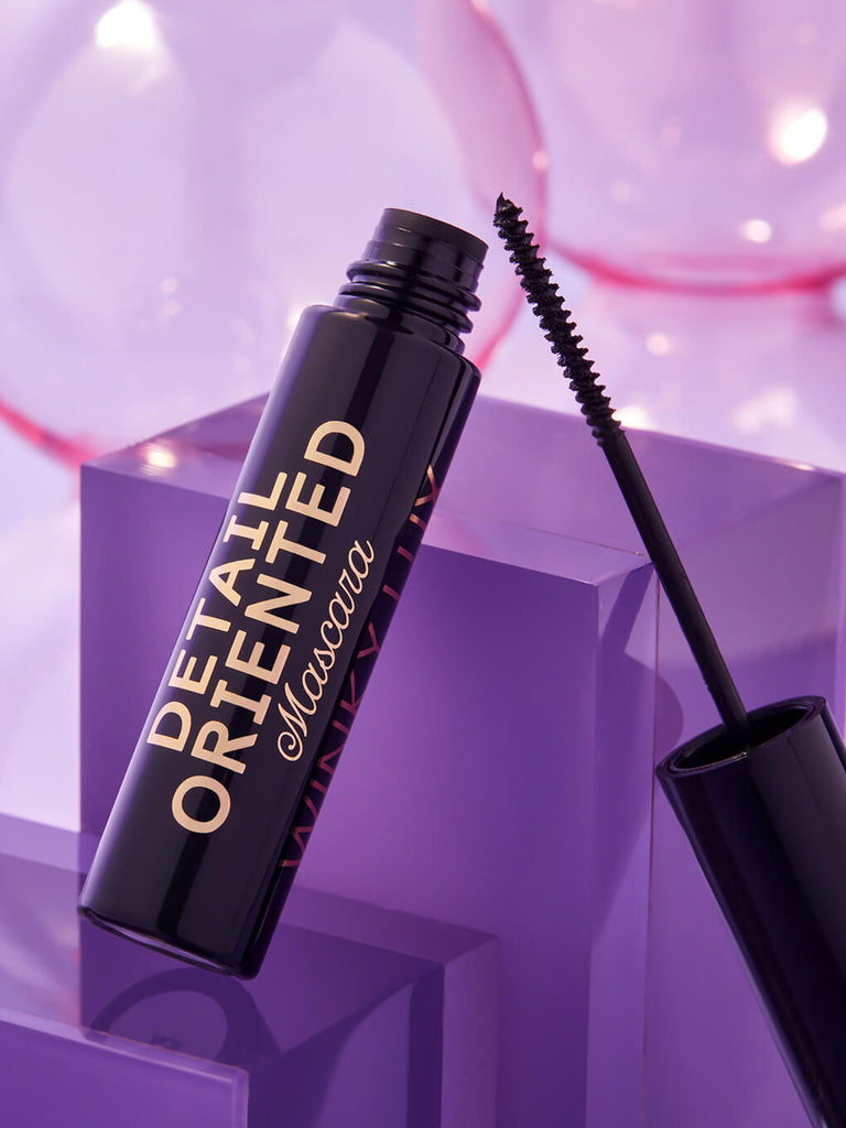 detail oriented mascara component opened and leaning on glass surface on purple background