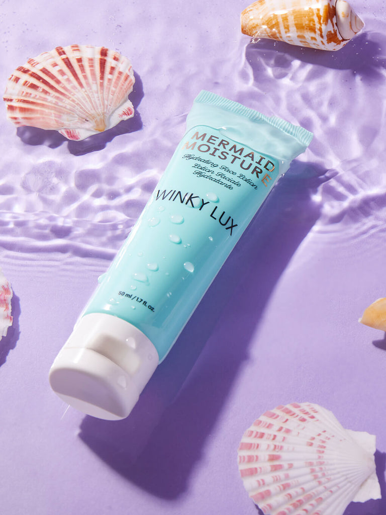 mermaid hydrating face lotion lying in shallow water with shells surrounding