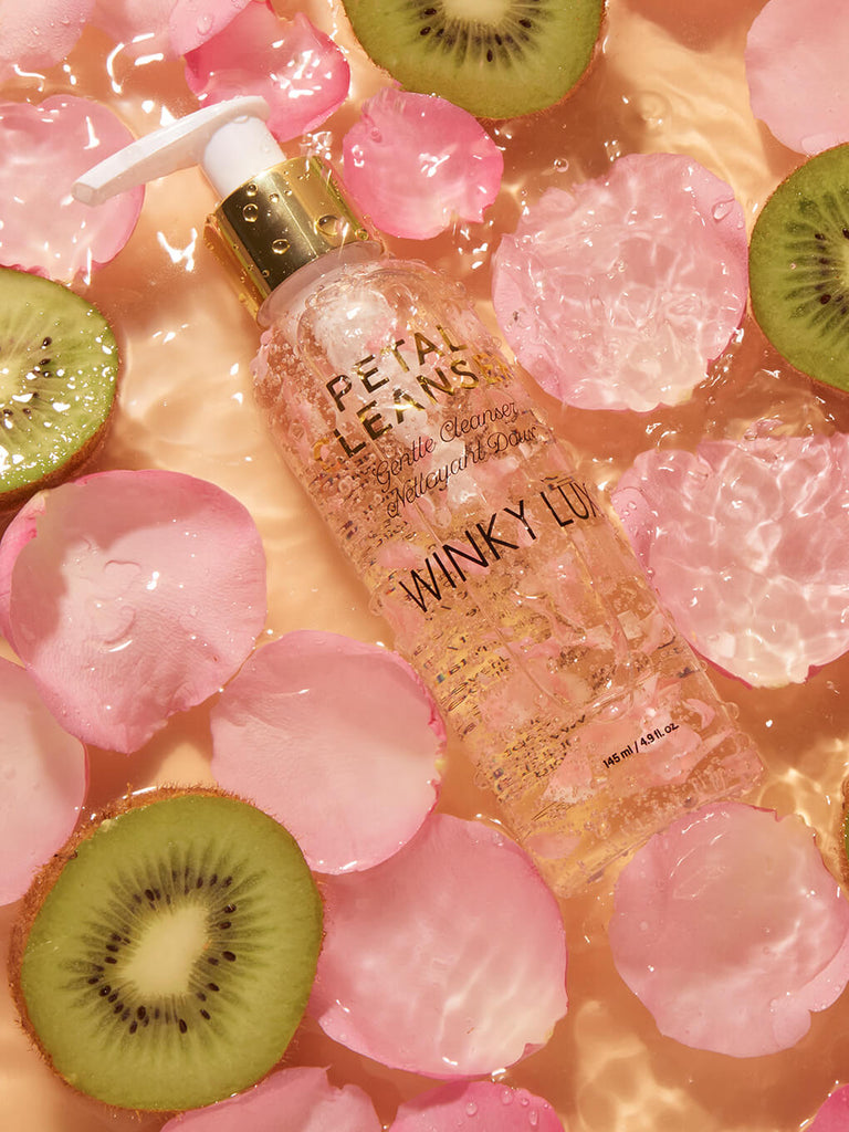 petal face cleanser flat lay in a bed of water with pink petals and kiwi surrounding