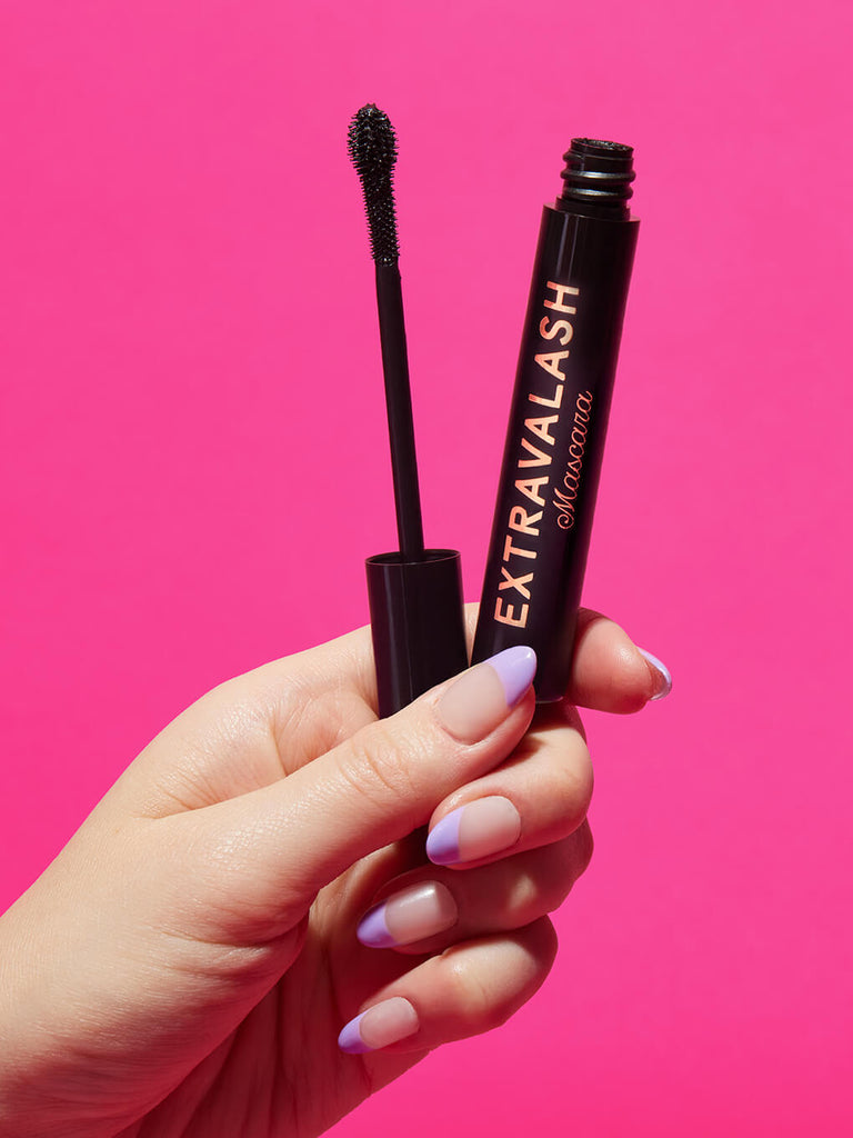 close up of model's hand holding extravalash mascara component wiht hot pink background