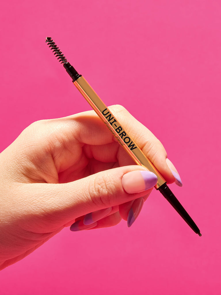 hand holding unibrow precision brow pencil on pink background