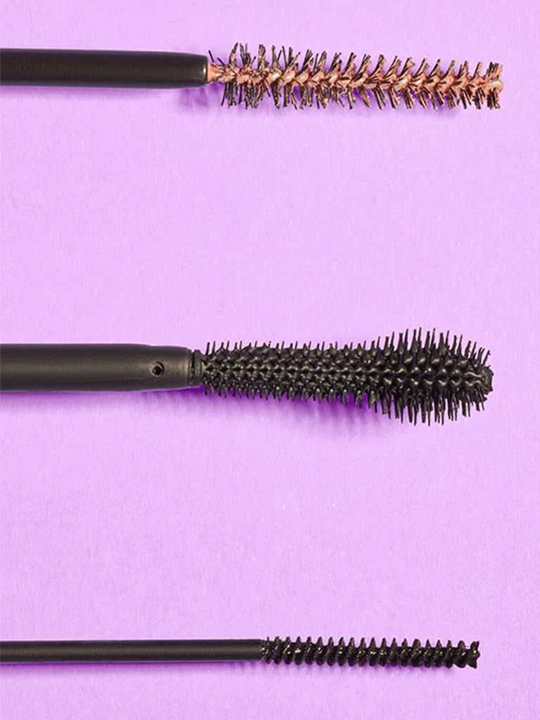 flat lay of tip of first swipe lash primer and two mascaras on purple background