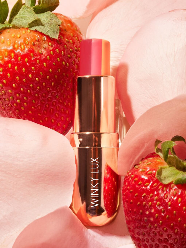 strawberry rose lip balm no cap resting in bed of rose petals and strawberries