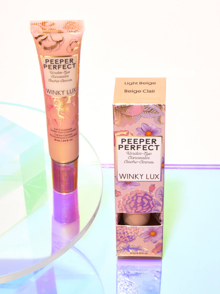 Light/Beige -- peeper perfect under eye concealer next to box with shiny props
